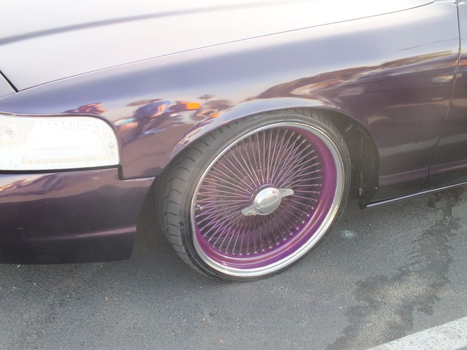 Close-up of a purple car's front fender and purple-spoked chrome wire wheel