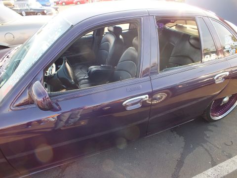 2003 Ford Crown Victoria - Side view of a glossy dark purple sedan with windows down, revealing a black leather custom interior and wire wheels.