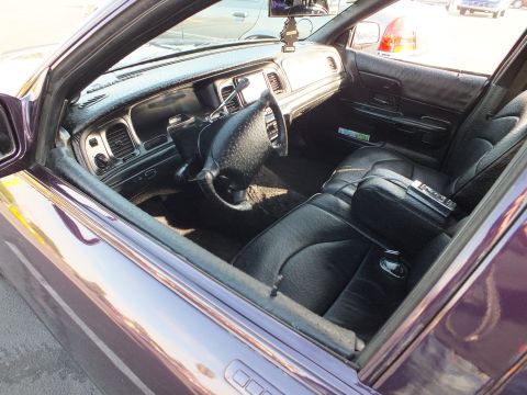 2003 Ford Crown Victoria - Interior of a dark sedan viewed through the side window, showing the dashboard, steering wheel and custom black leather seats.