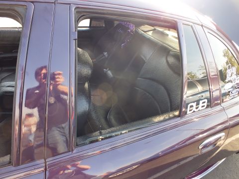 2003 Ford Crown Victoria - Rear side window of a glossy purple sedan bearing a DUB decal, with custom black leather rear seats visible inside.