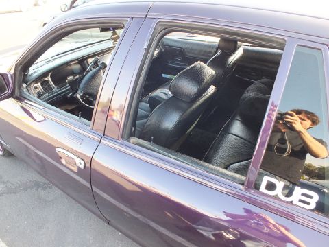 2003 Ford Crown Victoria - Side view of a glossy purple sedan, windows down, showing custom black leather seats and a DUB decal on the rear glass.