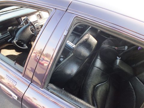 2003 Ford Crown Victoria - Custom black leather seats and dashboard of a purple sedan seen through the open rear side window.