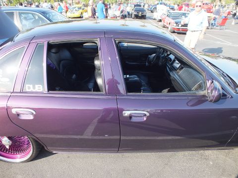2003 Ford Crown Victoria - close side view of a purple metallic sedan shows its black cloth interior through open windows and a white DUB decal on the glass.