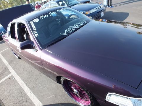 2003 Ford Crown Victoria - purple metallic sedan shows windshield lettering reading New Era Customs and Venom above its hood, riding on pink wire wheels.