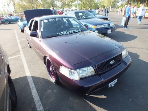 2003 Ford Crown Victoria - lowered purple Ford four-door sedan with a black mesh grille bearing the Ford oval sits in a show lot among other cars.