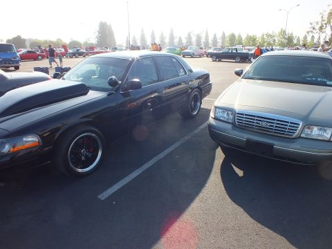 2003 Ford Crown Victoria - black full-size sedan parks alongside a silver-gray Ford Crown Victoria whose chrome grille carries the Ford oval emblem.