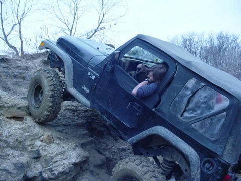 1992 Ford Bronco - A black Jeep Wrangler navigates a challenging rocky incline, with a person visible in the driver's seat.