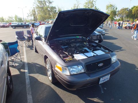 2003 Ford Crown Victoria - gray-purple Ford four-door sedan sits with its hood open over the engine bay, folding chairs and a crowd in the background.
