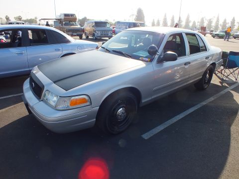 2003 Ford Crown Victoria - silver Ford Crown Victoria sedan with a matte black hood and black steel wheels parks beside a folding chair at the meet.