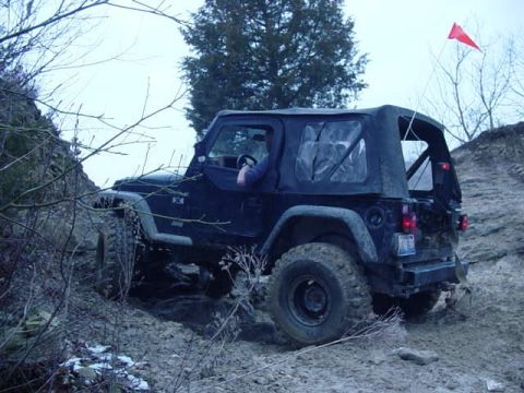 1992 Ford Bronco - Black Jeep Wrangler navigates a challenging off-road course on a cloudy day.
