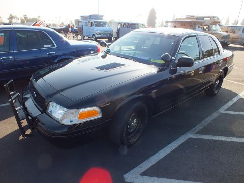 2003 Ford Crown Victoria - black Ford Crown Victoria fitted with a front push bar sits in a car-show parking lot near vintage vans.