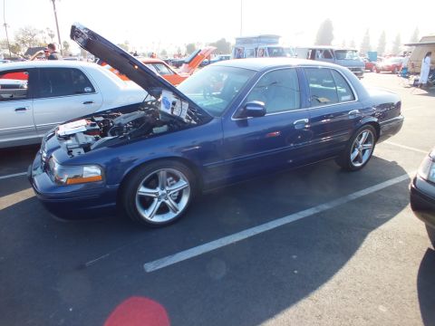 2003 Ford Crown Victoria - lowered dark-blue Mercury Marauder sedan shows its engine bay with the hood up at a sunny car show.