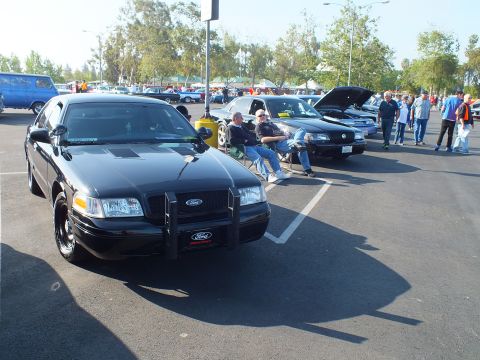 2003 Ford Crown Victoria - black Ford Crown Victoria Police Interceptor with a front push bar parks at a busy outdoor car show.