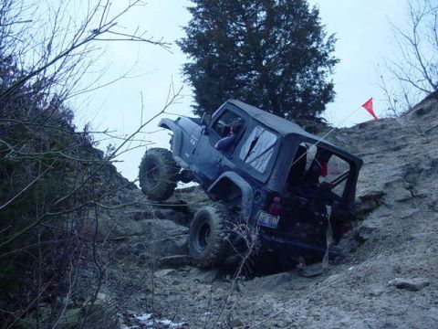 1992 Ford Bronco - A dark-colored Jeep Wrangler navigates a challenging off-road trail on a cloudy day.
