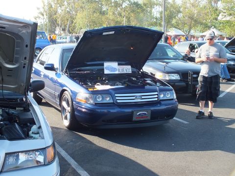 2003 Ford Crown Victoria - blue Ford Crown Victoria shows its engine bay with hood up and a BLUE VIC sign while a man stands alongside.