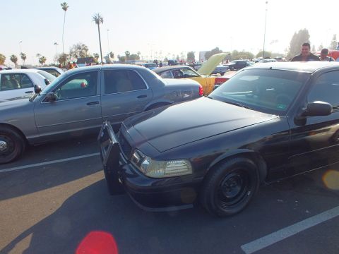2003 Ford Crown Victoria - black Ford Crown Victoria with a front push bar parks among many cars at a sunlit outdoor show.