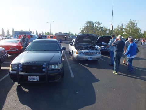 2003 Ford Crown Victoria - black Ford Crown Victoria with push bar and a silver Mercury with raised hood face the camera at a car show.