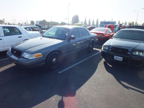 2003 Ford Crown Victoria - gray Ford Crown Victoria parks beside a black Crown Victoria with push bar at a sunlit car show.