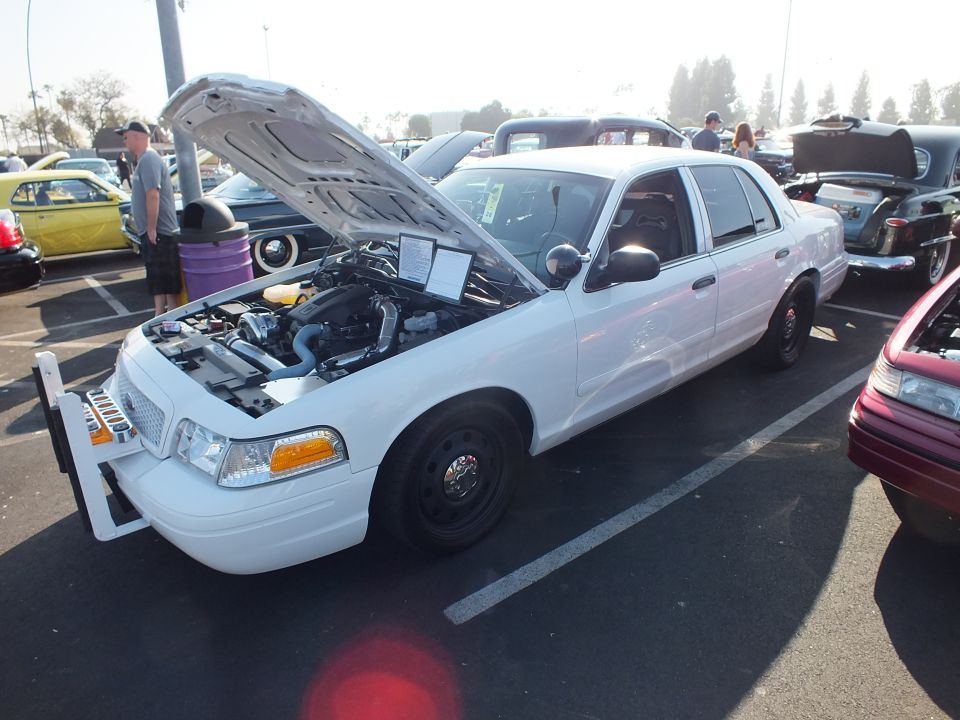 White Ford Crown Victoria with push bar and open hood at an outdoor car show