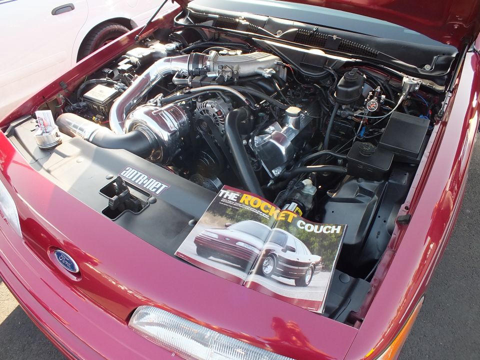 Red Ford engine bay with supercharger and a magazine page reading 'The Rocket Couch'