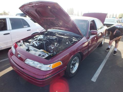 2003 Ford Crown Victoria - maroon Ford Crown Victoria sedan with its hood raised at an outdoor car show, a person crouching beside it.