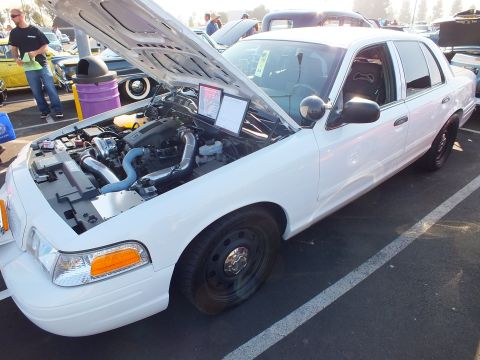 2003 Ford Crown Victoria - white Ford Crown Victoria sedan with hood up showing turbo plumbing and black steel wheels at a crowded car show.
