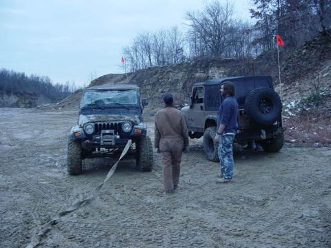 1992 Ford Bronco - Two Jeep Wranglers are in a dirt lot, one with a broken windshield, connected by a tow strap.