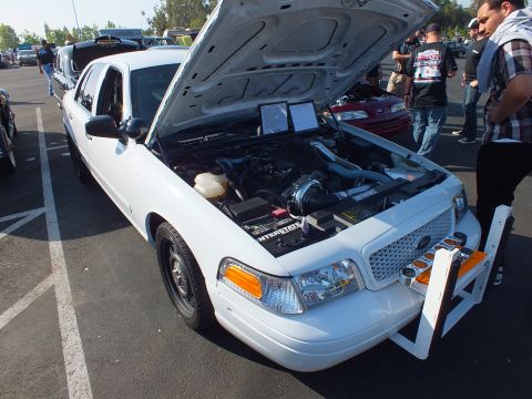 2003 Ford Crown Victoria - white Ford Crown Victoria with a chrome push bar and raised hood showing a turbo engine, a crowd gathered behind it.