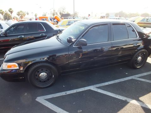 2003 Ford Crown Victoria - Side profile of a black Ford Crown Victoria sedan with black steel wheels and tinted windows parked in a lot at a car show.