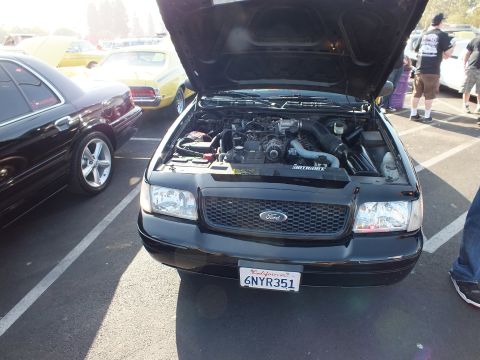 2003 Ford Crown Victoria - Front view of a black Ford with raised hood, mesh grille, and a California license plate reading 6NYR351 at a car show.