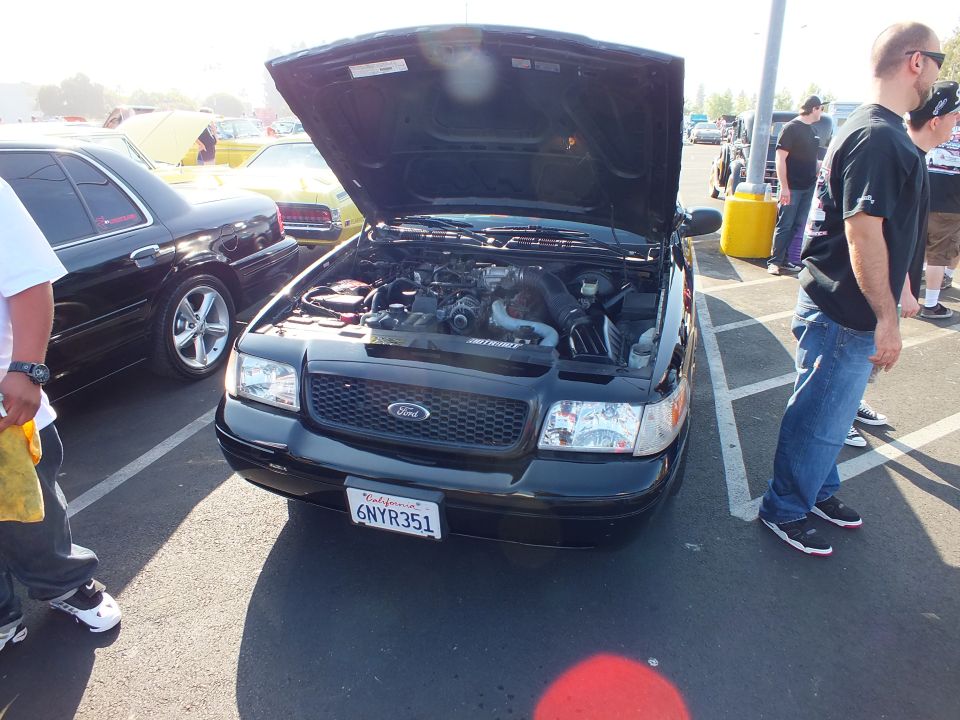 Black Ford with open hood and plate 6NYR351, spectators standing nearby