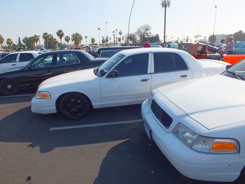 2003 Ford Crown Victoria - lowered white Ford Crown Victoria with black wheels parked beside another white sedan among rows of cars at an outdoor show.