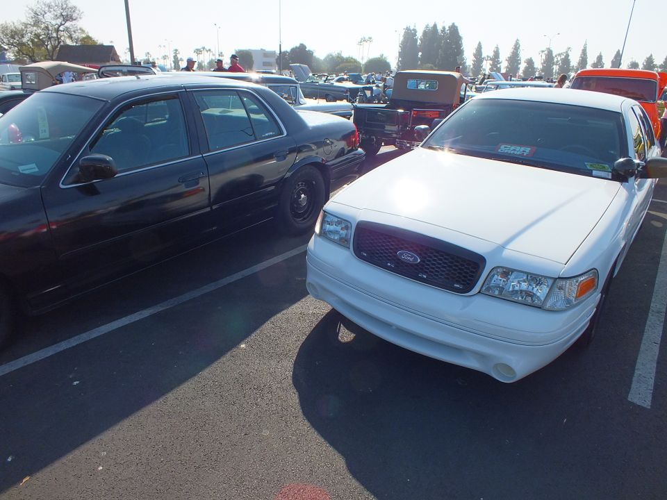 White Ford Crown Victoria with Ford grille beside a black sedan at an outdoor car show