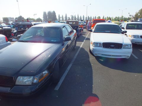 2003 Ford Crown Victoria - dark sedan parked next to a white Ford Crown Victoria with a body-color bumper among rows of cars at an outdoor show.
