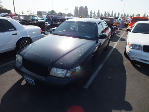 2003 Ford Crown Victoria - dark gray full-size sedan with a blacked-out grille and front plate parked among rows of cars in a sunny show lot.