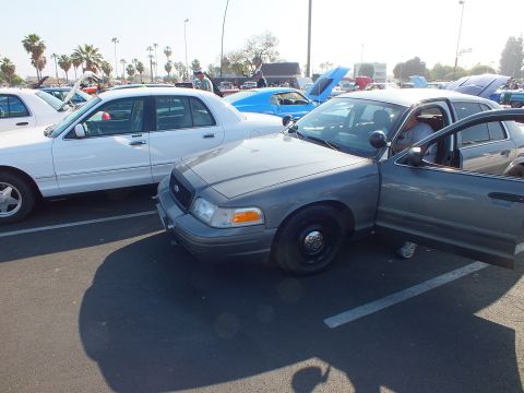 2003 Ford Crown Victoria - gray Ford Crown Victoria on black steel wheels parked at an angle beside a white sedan in a crowded show lot.