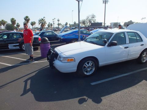 2003 Ford Crown Victoria - white Ford Crown Victoria missing its front bumper cover parked at a car show as a man in a red shirt stands beside it.