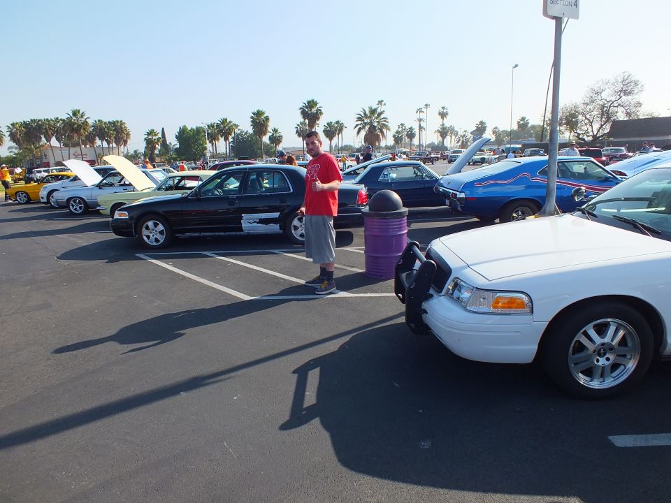 Man in red shirt standing between parked sedans at an outdoor car show