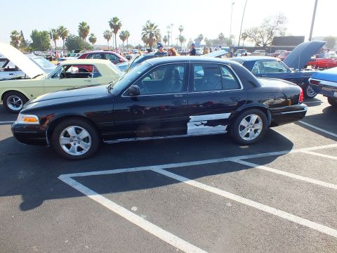 2003 Ford Crown Victoria - black Ford Crown Victoria shown in side profile on alloy wheels parked in a sunlit lot among classic cars.