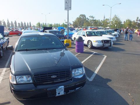2003 Ford Crown Victoria - black Ford Crown Victoria with a Ford grille badge parked nose-out as a white police-style sedan sits across the aisle.