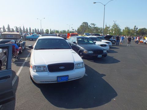 2003 Ford Crown Victoria - white Ford Crown Victoria with a front license plate parked nose-out among rows of cars and people at an outdoor show.