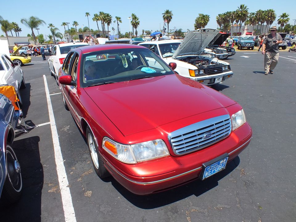 Red Ford sedan with chrome grille parked under palm trees at a car show