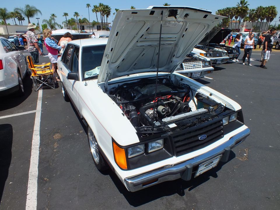 White Ford sedan with open hood showing engine at a car show