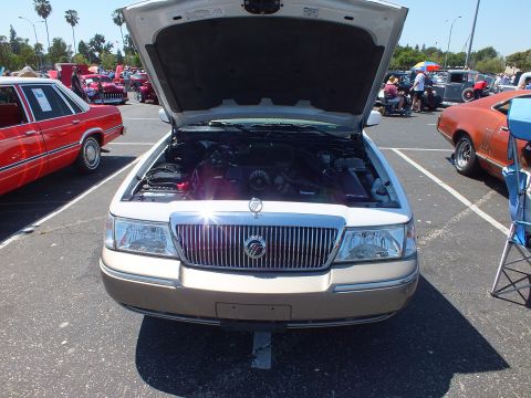 2003 Ford Crown Victoria - two-tone white and tan Mercury sedan shown head-on with chrome waterfall grille and raised hood at an outdoor show.