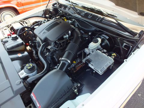 2003 Ford Crown Victoria - clean engine bay with black air intake, brake fluid reservoir and battery, hood raised beside an orange car.