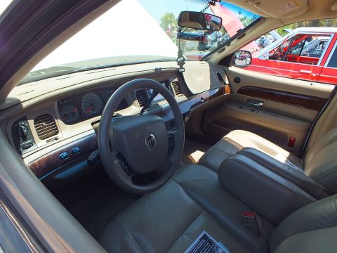 2003 Ford Crown Victoria - dashboard and steering wheel of a Mercury sedan with woodgrain trim, tan leather seats and a Mercury wheel emblem.