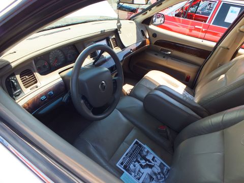 2003 Ford Crown Victoria - Mercury sedan interior with woodgrain dash and tan leather seats, an info flyer placed on the passenger seat.