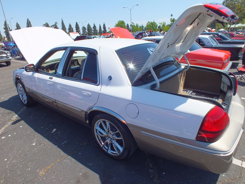 White and tan sedan with hood and trunk open at a sunny car show