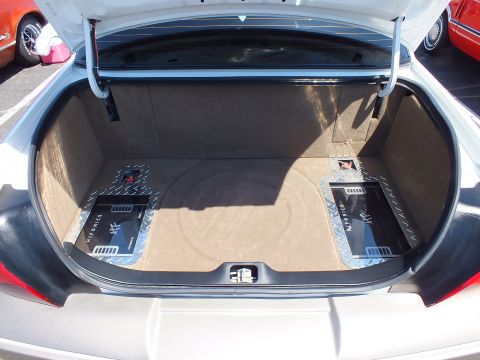 2003 Ford Crown Victoria - sedan trunk shows two amplifiers mounted on diamond-plate panels over carpeted flooring at a car show.