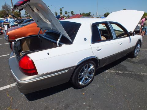 2003 Ford Crown Victoria - lowered two-tone white and tan sedan on chrome wheels seen from the rear, hood and trunk open at an outdoor show.